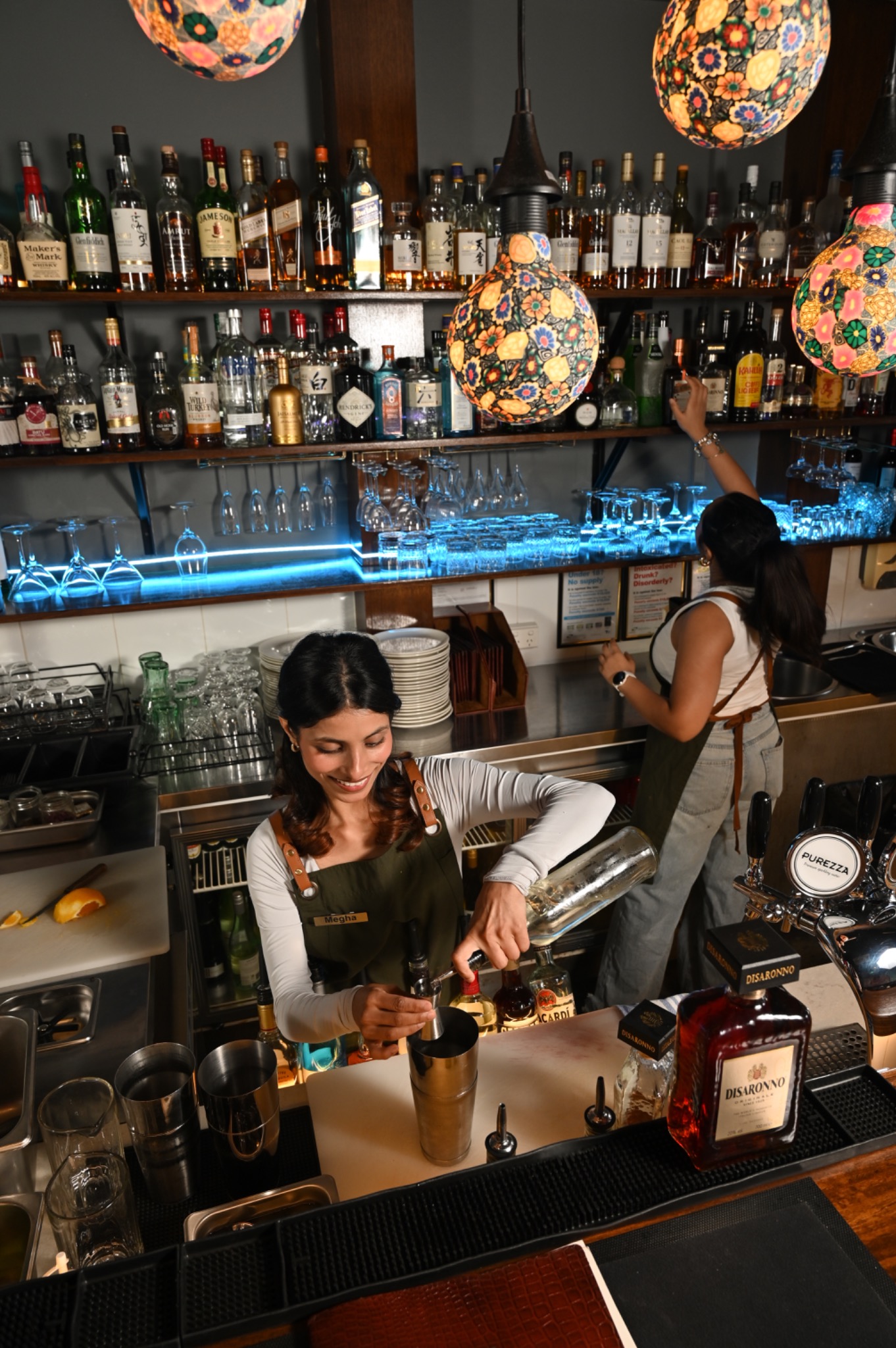 Our bartender preparing a cocktail beneath mosaic lamps