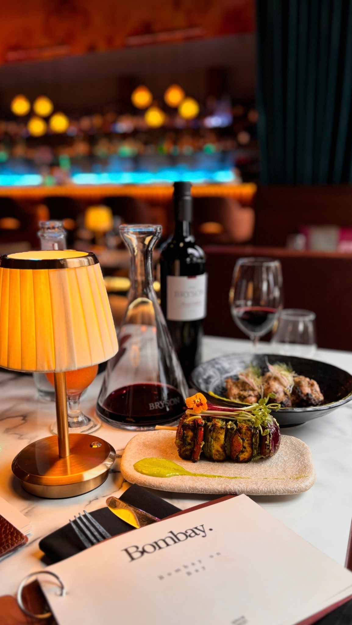 Paneer tikka, red wine and a golden lamp with the Bombay menu in the foreground