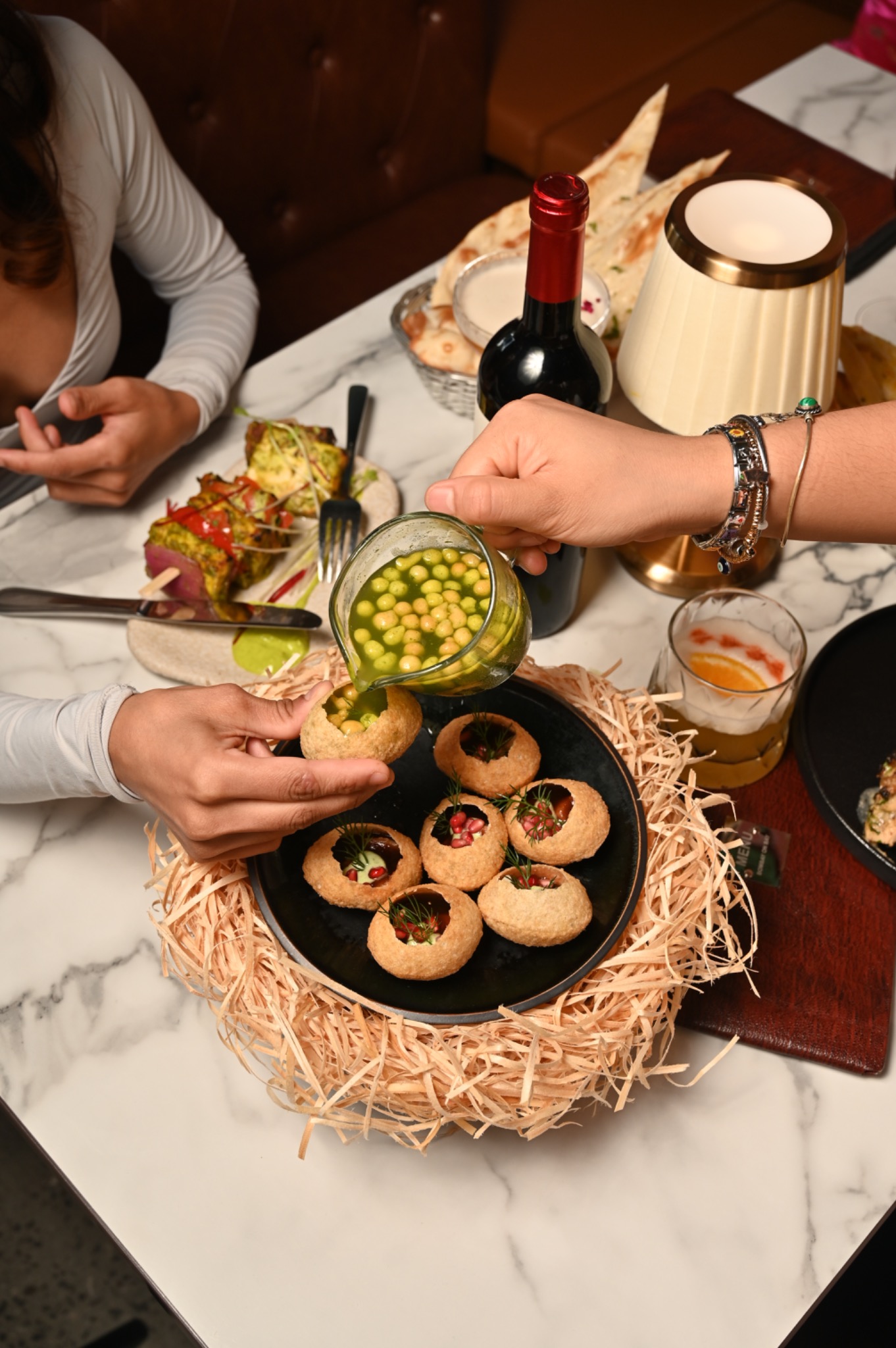 Guests pouring spiced pani into crisp puri shells at the table